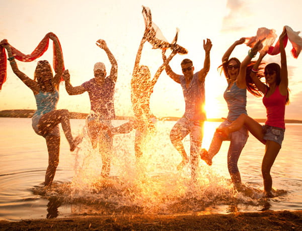A group of people jumping in the water at the beach during sunset.