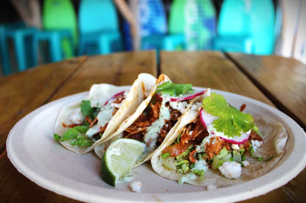 a plate of three tacos with meat, lime, cilantro, radish, and sour cream