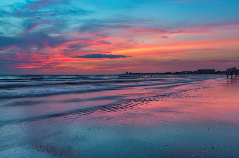 A beach at sunset with a vibrant sky and calm waves.