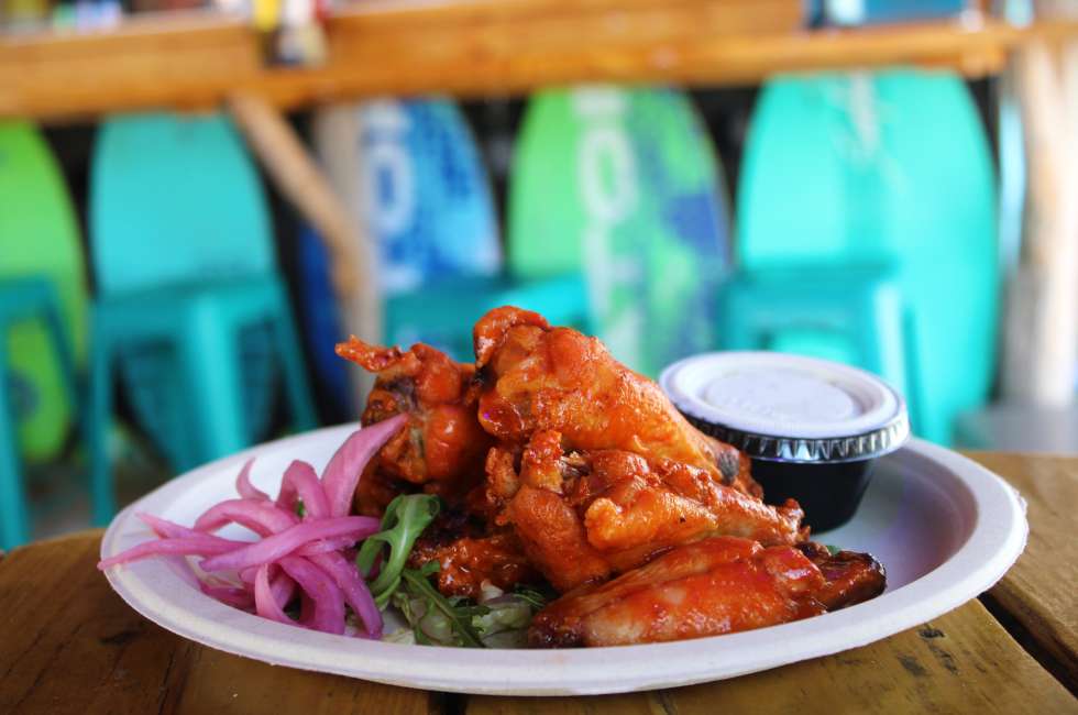 A plate of chicken wings with red sauce, pickled onions, and ranch dressing on a wooden table.