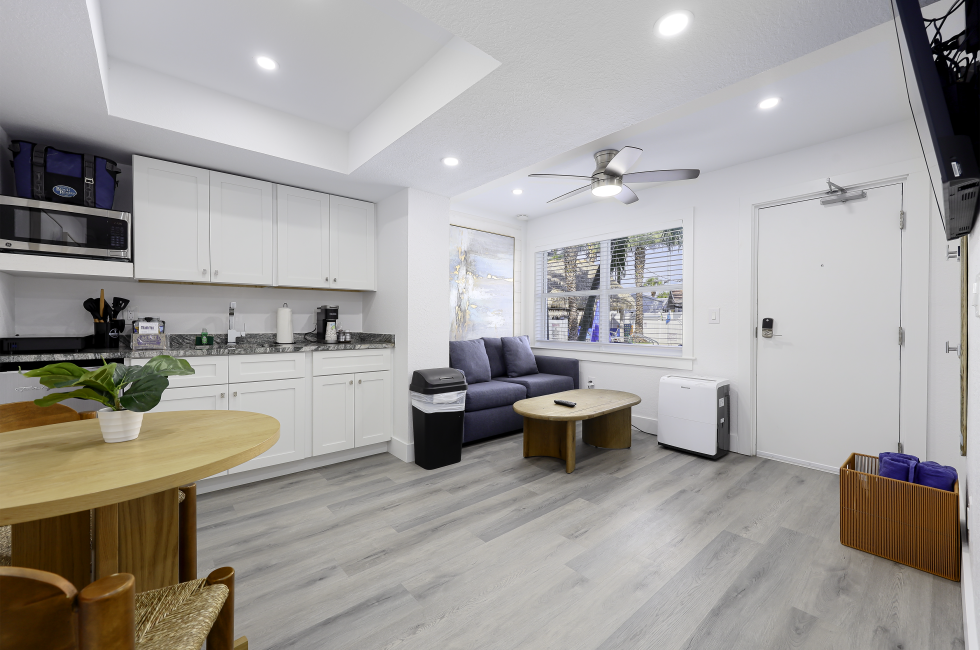 A brightly lit living room with kitchenette, sofa, coffee table, and dining table.
