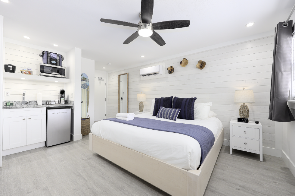 A wide-angle view of a hotel room with a bed, nightstands, and a small kitchenette.