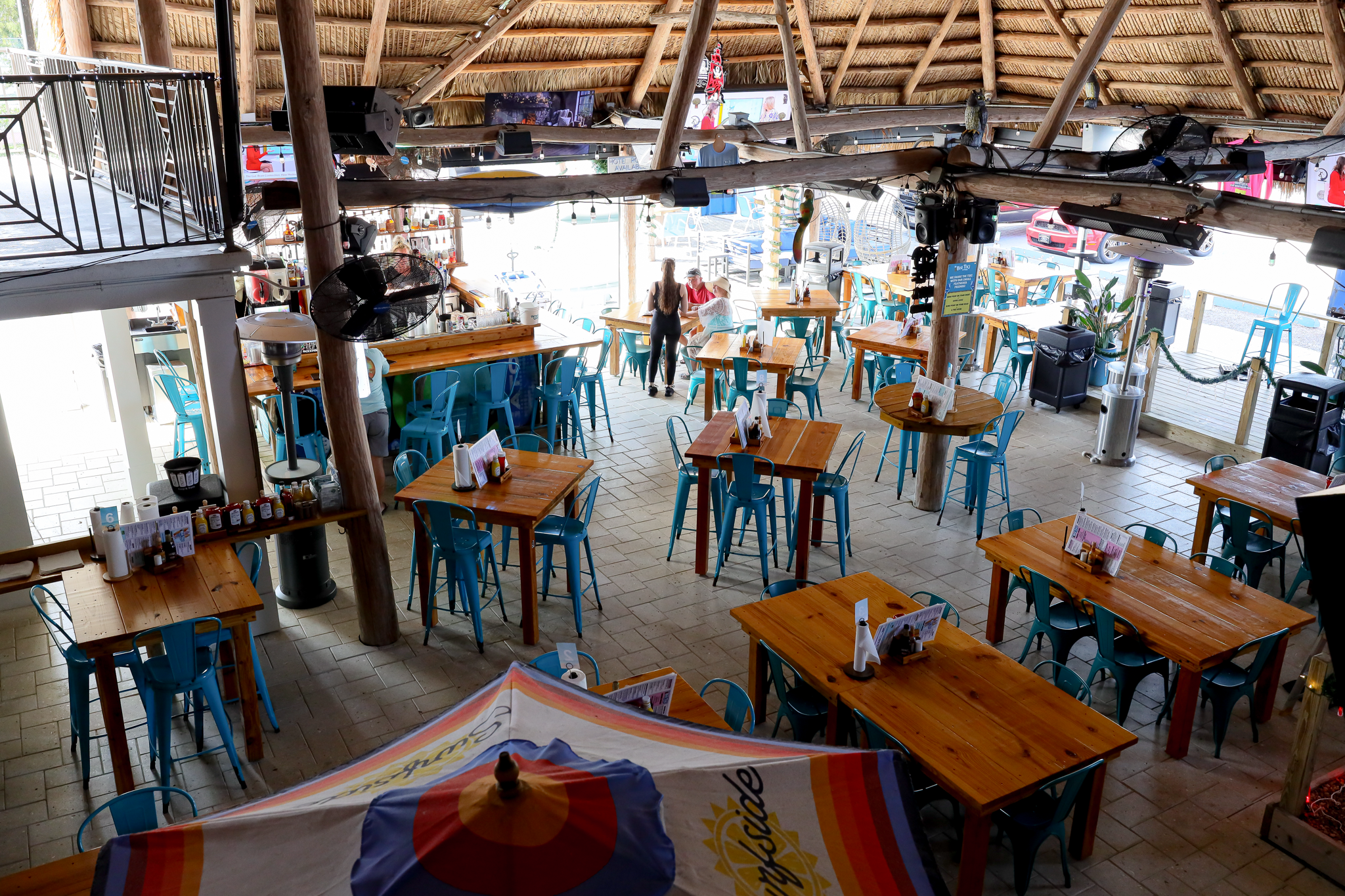 A dining area with wooden tables and blue chairs under a thatched roof.